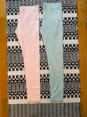 Två par leggings i pastellfärger (NYA!) - Helt nya och oanvända! Säljer två par mjuka leggings i pastellfärger, ett par i ljusrosa och ett par i ljusgrönt. Båda har hög midja och smal passform, perfekta för en avslappnad och trendig look. Materialet känns stretchigt och bekvämt, utan synliga loggor eller detaljer.