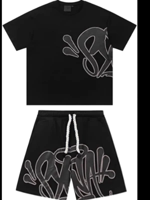 Svart set med graffiti-tryck - Säljer ett svart tvådelat set med t-shirt och shorts. Båda delarna har ett stort, grått graffiti-inspirerat tryck och vita snören i midjan på shortsen. Setet har en avslappnad passform och är gjort i mjukt material, perfekt för en chill look.