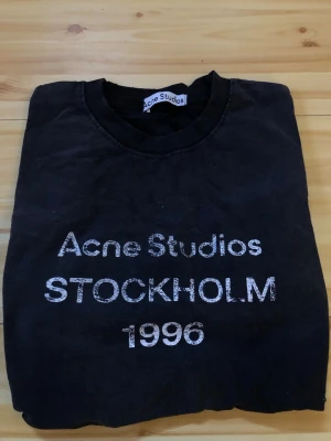 Svart Acne Studios t-shirt Stockholm - Säljer en svart t-shirt från Acne Studios med trycket 'Acne Studios STOCKHOLM 1996' på framsidan. Klassisk rund hals och korta ärmar. Perfekt för dig som gillar stilrena och ikoniska plagg med streetwear-vibe.