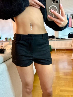 Svarta shorts med bälteshällor - Säljer ett par svarta shorts med bälteshällor och klassisk passform. Materialet är väldigt mjukt och lätt, vilket gör dem sköna att bära. Enkla att matcha med olika toppar för en clean look. 