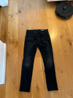 Svarta Replay jeans Hyperflex - Säljer ett par svarta jeans från Replay med raka ben.Jeansen har diskreta slitningar och är tillverkade i bomull med lite stretch för skön passform. Perfekta för en avslappnad men snygg stil. Använda ett fåtal gånger.