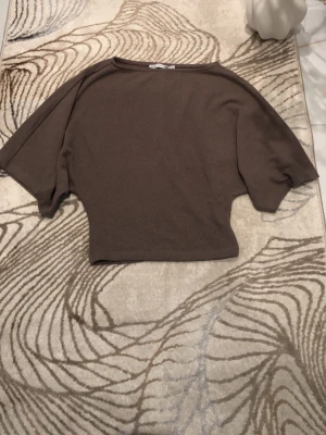 Brun loose topp med vida ärmar - Säljer en brun topp med loose passform och vida, korta ärmar. Toppen har en enkel, stilren design och är tillverkad i ett mjukt material som känns skönt mot huden. Perfekt för dig som gillar avslappnad stil. Använd endast en gång. Är öppen med prisförslag😊