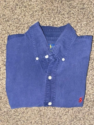 Blå Ralph Lauren skjorta - Blå Ralph Lauren skjorta i storlek S med slim fit-passform. Något använd, små defekter i armhåleområdet men syns knappt. Be om fler bilder för att se. skick 8/10