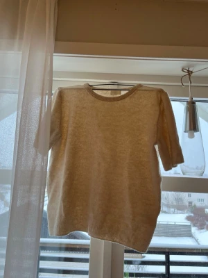 Beige stickad tröja med kort ärm - Mysig beige stickad tröja med korta ärmar och rund halsringning. Tröjan har en enkel och stilren design, perfekt att matcha med jeans eller kjol. Materialet är mjukt och bekvämt, och modellen är rak med ribbstickade kanter.🫶🏼