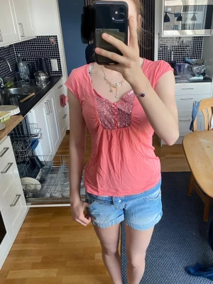 Rosa topp med paljettdetalj - Söt rosa topp med korta ärmar och v-ringning. Jag tror att jag har köpt den begagnad men den ör i bra skick. Jag själv har använt den ingen gång. Jag hade gärna haft kvar den men jag måste rensa min garderob. Frakt ingår inte i det skrivna priset. Storleken är i cambodiansk storlek i svensk storlek skulle jag säga S-M