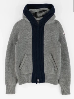 Grå stickad hoodie från Moncler - Säljer en grå stickad cardigan från Moncler med mörkblå ribbstickad kant längs dragkedjan och huvan. Tröjan har två fickor fram, Moncler-logga på ärmen och ribbade muddar, för mer info och bilder skriv till mig! 10/10 skick och självklart äkta!!!