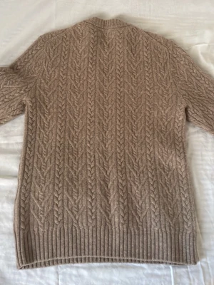 Beige kabelstickad tröja från C&A - Säljer en beige kabelstickad tröja från C&A med rund halsringning och ribbade muddar vid ärmslut och nederkant. Tröjan har ett snyggt flätmönster över hela plagget och är perfekt för dig som gillar klassisk och stilren design.