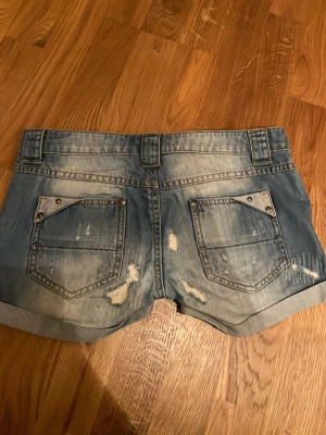 Blå coola jeansshorts - Säljer ett par blå jeansshorts med slitningar och uppvikta benslut. Shortsen har fem fickor, bälteshällor och detaljerade slitningar både fram och bak för en trendig look. Perfekta för dig som gillar en avslappnad och cool stil.