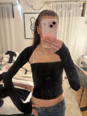 Svart croppad topp med öppen rygg - Trendig svart croppad topp med lång ärm och liten öppen rygg. Toppen har en tight passform och fyrkantig ringning framtill. Nästan aldrig använd. 