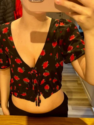 Blommig croppad topp - Jättefin mönstrad tröja🌺. Snörning framtill ( kan välja att ha den öppen ). Är egentligen en knapp under snörningen men den har tyvärr lossnat. Ganska så urringad, jag har vid mer formella tillfällen använt en säkerhetsnål för att göra urringningen mindre. Tror den är köpt på Zalando, märket Brave Soul.
