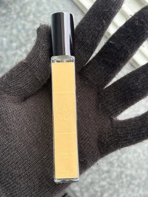 Kayali Vanilla 28 parfym - Kayali Vanilla 28 är en elegant parfym i en smal, rektangulär glasflaska med svart lock. Etiketten är beige med guldtext. Doften har tydliga inslag av vanilj och flaskan rymmer 10 ml, perfekt att ha med i väskan.