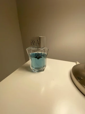 Armani parfym med blått innehåll - Säljer en parfym från Armani med fräscht blått innehåll. Flaskan är tillverkad i genomskinligt glas med en elegant, kantig form och har ett silverfärgat lock med dekorativa detaljer. Perfekt för dig som gillar stilrena och moderna dofter.