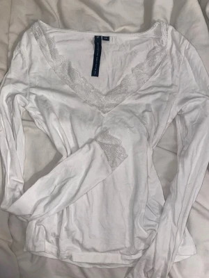 Vit långärmad topp med spets - Säljer en vit långärmad topp från H&M med v-ringning och fina spetsdetaljer vid halsringningen och ärmsluten. Tillverkad i mjuk bomull som känns skön mot huden. Perfekt för dig som gillar en enkel men söt stil.