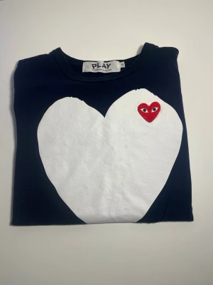 Comme des Garçons Play hjärttshirt - Mörkblå t-shirt från Comme des Garçons Play med stort vitt hjärta och det klassiska röda hjärtat med ögon broderat på bröstet. T-shirten har rund hals och är kortärmad. Tillverkad i mjuk bomull för skön känsla. As fet T-shirt! Är i stolek S men passar Xs oxå! Skick 8/10