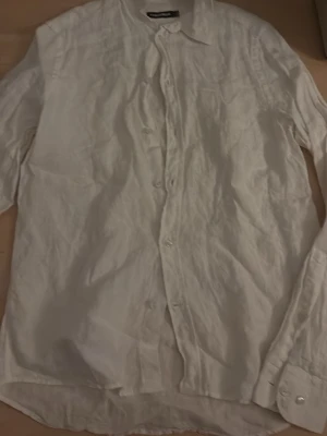 Vit linneskjorta  J Lindeberg - Klassisk vit skjorta från JL luftigt linne. Skjortan har lång ärm, knappar framtill och en avslappnad passform. Perfekt till sommaren och enkel att styla med olika outfits.