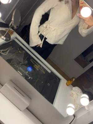 Krämvit omlottkofta med knytband - Mysig krämvit omlottkofta med långa ärmar och knytband i midjan. Koftan har en djup v-ringning och är tillverkad i ett mjukt, stickat material som känns skönt mot huden. Perfekt för lager-på-lager och enkel att styla till olika outfits.