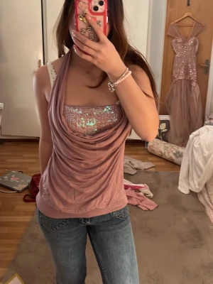 Rosa halterneck topp med paljetter - Säljer en snygg rosa halterneck topp med draperad front och glittriga paljetter över bysten. Toppen är ärmlös och har en croppad känsla, perfekt för dig som vill sticka ut. Materialet känns mjukt och stretchigt, troligen polyester.