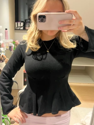 Svart långärmad topp med volang - Snygg svart långärmad topp med volang nertill och figurnära passform. Toppen har rund halsringning och är tillverkad i ett stretchigt material som sitter bekvämt. Perfekt att styla med både jeans och kjol.