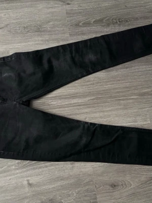 Svarta skinny jeans från nudie jeans  - Säljer ett par svarta skinny jeans från .nudie jeans med klassisk femficksdesign och smal passform. Jeansen har bälteshällor och är tillverkade i stretchigt material för extra komfort. Perfekta för en clean och stilren look.