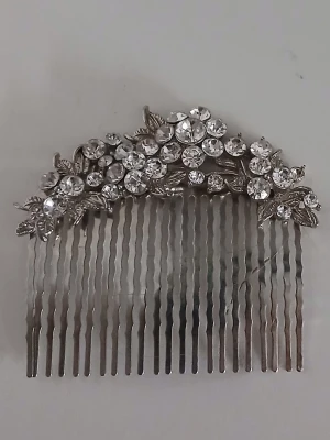 Silverfärgad hårkam med strassblommor - Snygg hårklämma i silverfärgad metall dekorerad med gnistrande strass i blomform och små detaljerade blad. Perfekt för att ge frisyren extra bling och en elegant touch. Passar till dig som vill sticka ut med accessoarer som verkligen syns.