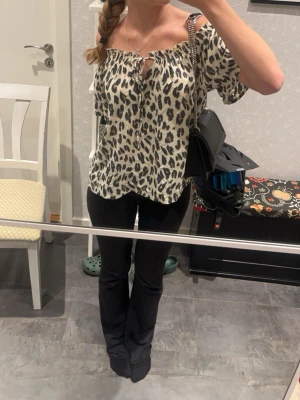 Leopardmönstrad offshoulder topp - Säljer en snygg offshoulder topp med leopardmönster i svart och beige. Toppen har korta ärmar, knytning framtill och en avslappnad passform.