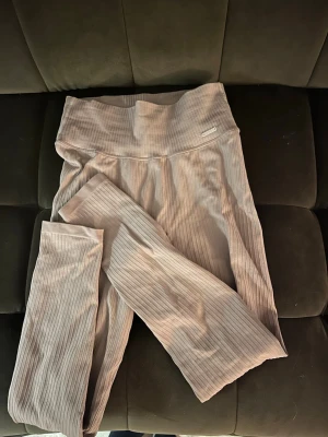 Beige ribbade leggings från Aim'n - Supersnygga beige leggings från Aim'n i ribbat stretchigt material. Hög midja och diskret metallogo framtill. Perfekta för en chill och sportig look, matcha med crop top eller hoodie. Materialet är mjukt och följsamt, vilket gör dem riktigt bekväma.