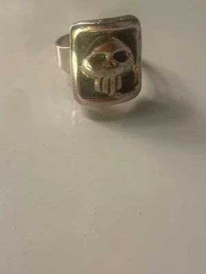 Silvrig ring med dödskallemotiv - Cool ring i silverfärgad metall med ett rektangulärt ansikte och ett upphöjt dödskallemotiv. Ringen har en robust känsla och en unik design som sticker ut. Perfekt för dig som gillar alternativa accessoarer och vill ha något som syns. 