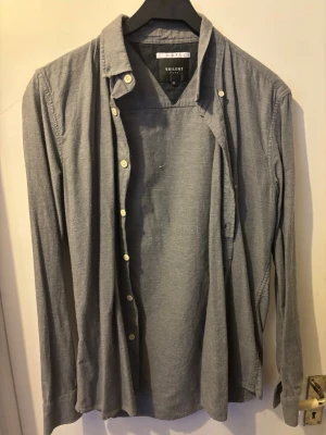 Grå skjorta från Vailent - Säljer en stilren grå skjorta från Vailent med klassisk krage och vita knappar. Skjortan är långärmad och har en enkel, clean look som passar till många olika outfits. Tillverkad i mjuk bomull för skön känsla.