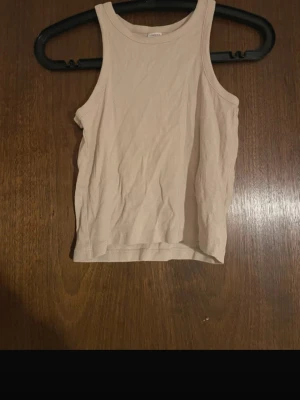 Beige ribbad linnetopp - Snygg beige ribbad linnetopp med rund halsringning. Perfekt att styla med jeans eller kjol för en enkel och trendig look. Ärmlös och i mjukt material som känns skönt mot huden.