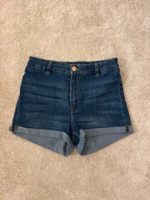 Blå denimshorts med uppvik - Klassiska blå jeansshorts med uppvikta benslut och femficksdesign. De har normal passform, bälteshällor och stängs med knapp och dragkedja. 