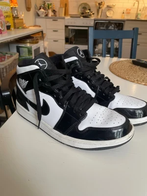 Air Jordan 1 Mid svart/vit - Säljer ett par Air Jordan 1 Mid sneakers i svart och vitt med klassisk Nike Swoosh och Air Jordan-logga på sidan. Skorna har svarta skosnören, vit tåbox och svart glansig finish på vissa partier. Perfekta för dig som gillar streetwear och ikonisk design. Priset kan diskuteras 
