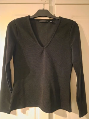 Svart långärmad v-ringad topp - En stilren svart långärmad topp från H&M med v-ringning. Toppen har en enkel och klassisk design som passar till många olika outfits. Materialet känns mjukt och stretchigt, vilket gör den bekväm att bära.