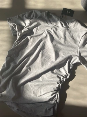 Tränings t shirt med snörning  - Snygg mjuk grå tränings- t shirt. T-shirten har korta ärmar och cool snörningsdetalj på sidan som ger en unik twist. Perfekt till ett träningspass eller bara i vardagen!