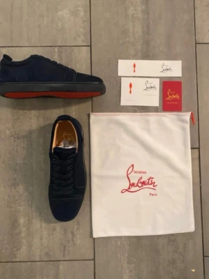 Mörkblå sneakers från Christian Louboutin - Snygga mörkblå sneakers från Christian Louboutin i mocka med klassisk röd sula och diskret logga på sidan. Skorna har svarta snören och en låg silhuett som ger en clean och exklusiv look. Kommer med originalpåse och tags.