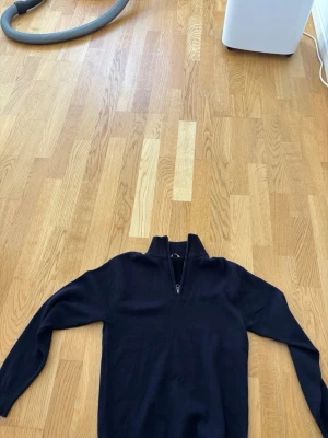 Mörkblå stickad tröja med halvzip - Mörkblå stickad tröja med halv dragkedja och hög krage. Tröjan har långa ärmar och ribbade muddar vid ärmslut och nederkant. Perfekt för lager-på-lager och enkel att matcha med jeans.