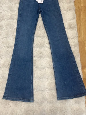 Blå bootcut jeans - Säljer ett par klassiska blå bootcut jeans i mjuk denim med utsvängda ben. Helt nya med prislapp. Köptes för 500kr