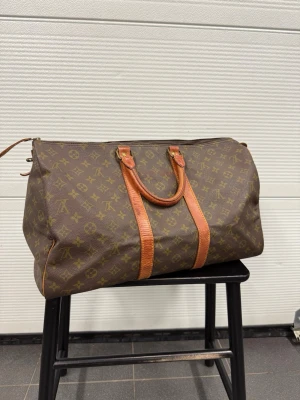 Louis Vuitton Keepall 45 - En väska från Louis Vuitton modell keepall i fint vintage skick! Den är i storlek 45 och har måtten 45x27x20cm. På insidan finns en text överstruken med tusch. Finns även nå mindre märken men fint helt hets skick! Självklart äkta kommer med äkthetslapp från The Grand Closet! Hör av er vid frågor! 