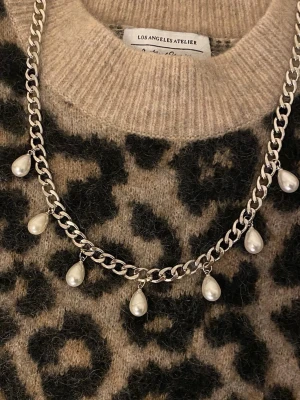 Silverfärgat halsband med pärlor - Snyggt halsband rostfritt stål med kraftig silverfärgad kedja och hängande droppformade pärlor. Perfekt för att ge din outfit en cool och trendig touch. Materialet är metall och pärlorna är vita och glänsande.