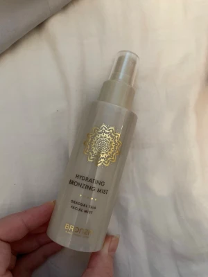 Hydrating Bronzing Mist från BRONZR - Ny Hydrating Bronzing Mist från BRONZR är en ansiktsmist som ger en gradvis solkysst ton. Flaskan är beige med gulddetaljer och har en sprayfunktion för enkel applicering. Perfekt för dig som vill ha en naturlig glow utan sol. Innehåller återfuktande ingredienser.