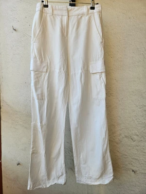 Vita linnebyxor med fickor - Vita linnebyxor i cargomodell från H&M. Storlek 34. Två framfickor och tre på sidan, fickorna på baksidan är inte riktiga. Lite slitna nedtill som man ser på sista bilden.