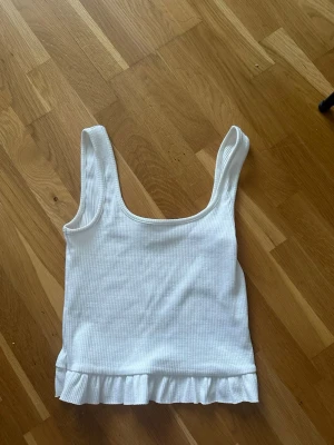 Vit ribbad linnetopp med volangkant - Söt vit ribbad linnetopp med breda axelband och volangkant längst ner. 