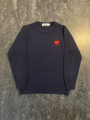 Mörkblå stickad tröja Comme des Garçons - (Priset går att diskuteras) Mörkblå stickad tröja från Comme des Garçons PLAY med det ikoniska röda hjärtat broderat på bröstet. Perfekt för dig som gillar stilrena plagg med en twist.