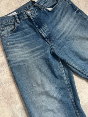 Blåa jeans - Säljer ett par blå jeans med wide/ rak passform och snygg vintage tvätt. Jeansen har klassisk femficksdesign, normal midja och slitningar för en cool, avslappnad look. Perfekta till sneakers och hoodie. Materialet är 100% bomull.
