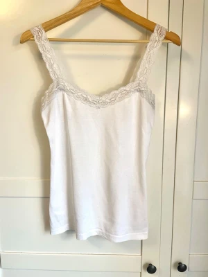 Vit linnetopp med spetsdetaljer - Snygg vit linnetopp med breda axelband från Odd Molly med dekorativ spets längs halsringningen och axelbanden. Toppen är enkel och feminin, perfekt att matcha med jeans eller kjol. Liten broderad detalj baktill. Materialet känns mjukt och bekvämt.