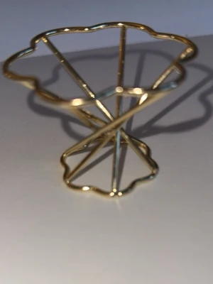 Guldfärgad hållare för sminksvamp - Stilren hållare i guldfärgad metall, perfekt för att förvara och torka din sminksvamp. Den har en vågig, öppen design som ger bra ventilation och passar snyggt på sminkbordet. Praktisk och dekorativ detalj för din skönhetsrutin.