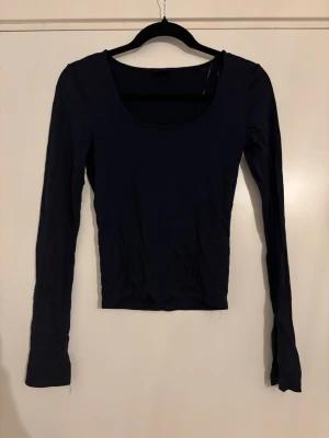 Svart långärmad topp med rund hals - En enkel och stilren svart långärmad topp med rundad urringning. Toppen har en tight passform och är perfekt att matcha med olika outfits. Tillverkad i mjukt material som känns skönt mot huden.