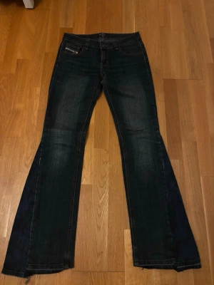 Diesel jeans - Säljer ett par mörkblå omsydda bootcut jeans. Jeansen har en låg midja och vida ben, perfekta för en avslappnad och trendig look. Materialet är denim i bomull med lite stretch för extra komfort.