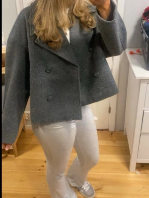 Grå ullrock från 157, dubbelknäppt - Snygg grå rock från 157 i ullblandning med dubbelknäppning och bred krage. Modellen är boxig och lite kortare, vilket ger en modern och trendig look. 