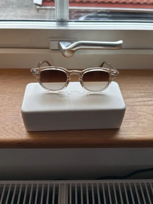 Core 01 solglasögon från Chimi - Snygga solglasögon från chimi, modell Core 01. Glasögonen har transparenta beige bågar och bruna tonade linser. Stilen är modern och passar dig som gillar en clean look. Kommer med ett vitt fodral med chimi-logga. Använda endast 2 gånger 