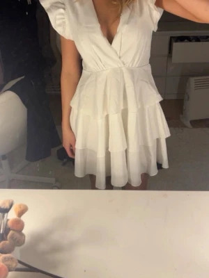 Vit volangklänning med v-ringning - Supersöt vit klänning med flera volanger och v-ringad omlottfront. Puffiga korta ärmar och markerad midja. Perfekt för sommarens alla tillfällen och studenten! Från Boohoo. 